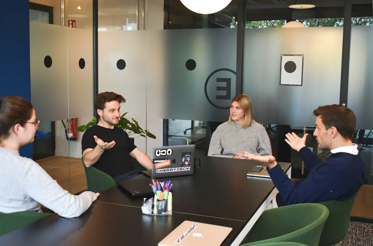 Agência ou freelancer de tráfego pago: equipe em reunião de trabalho ao redor de uma mesa com notebooks em escritório moderno.