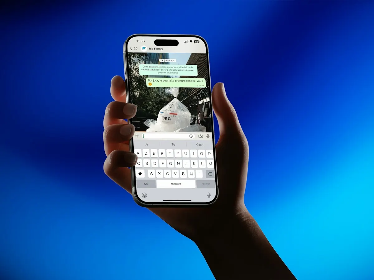 Mão segurando um celular com uma conversa de WhatsApp com uma empresa aberta e o teclado na tela, sobre fundo azul.