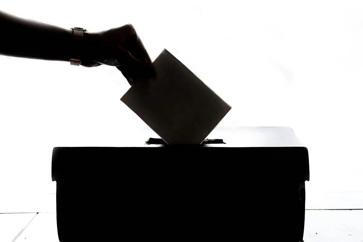 Silhueta de mão depositando um voto na urna, ilustrando a apuração das eleições 2026.