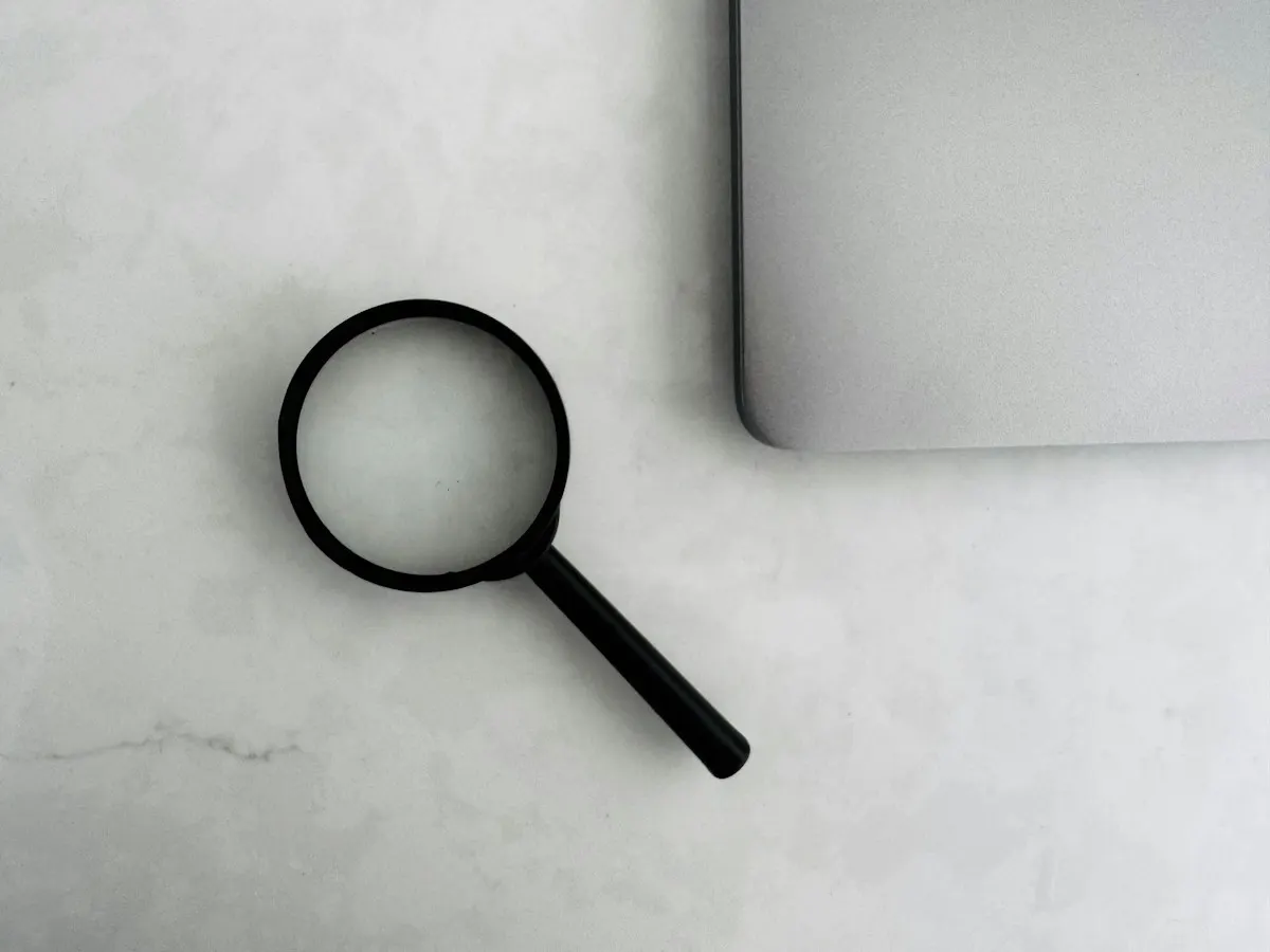 Lupa ao lado de um notebook sobre mesa clara, representando o diagnóstico de SEO para IA e a medição das respostas.