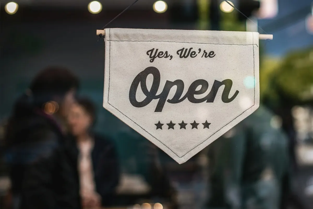 Placa pendurada na entrada de um estabelecimento com a frase “Yes, we’re open”, avisando que está aberto.