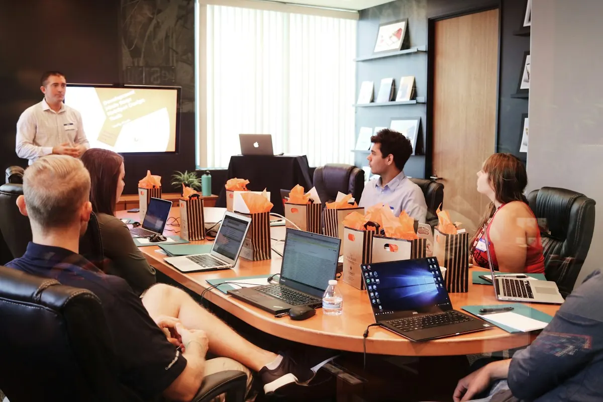 Homem apresentando em reunião de escritório para equipe com notebooks ao redor da mesa.
