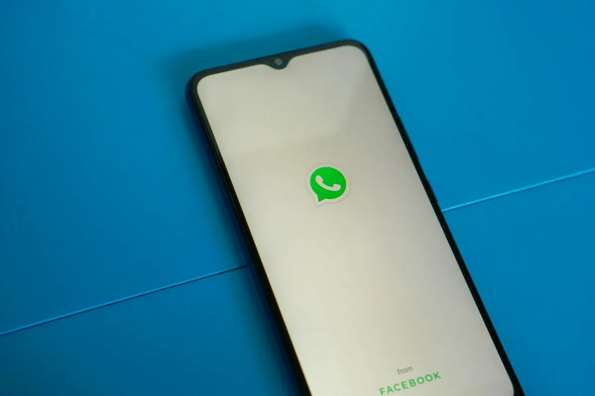 Celular apoiado sobre uma superfície azul, com o ícone verde do WhatsApp na tela de abertura do aplicativo.