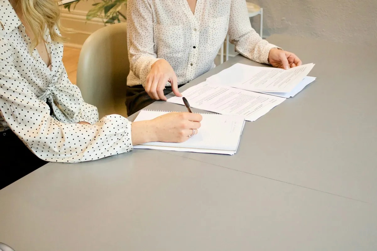 Pessoas revisando e assinando documentos em uma mesa, representando o acordo de acessos e ownership da conta de anúncio.