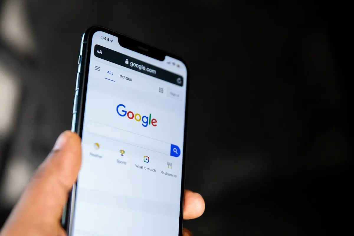 Mão segurando um smartphone com a página inicial da busca do Google aberta, pronta para uma pesquisa local.