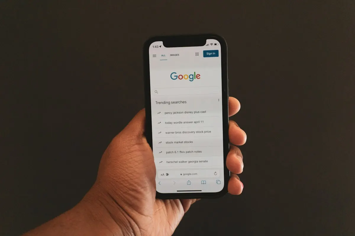 Mão segurando um celular com a página inicial do Google aberta, representando a busca pelo Perfil da Empresa no Google.