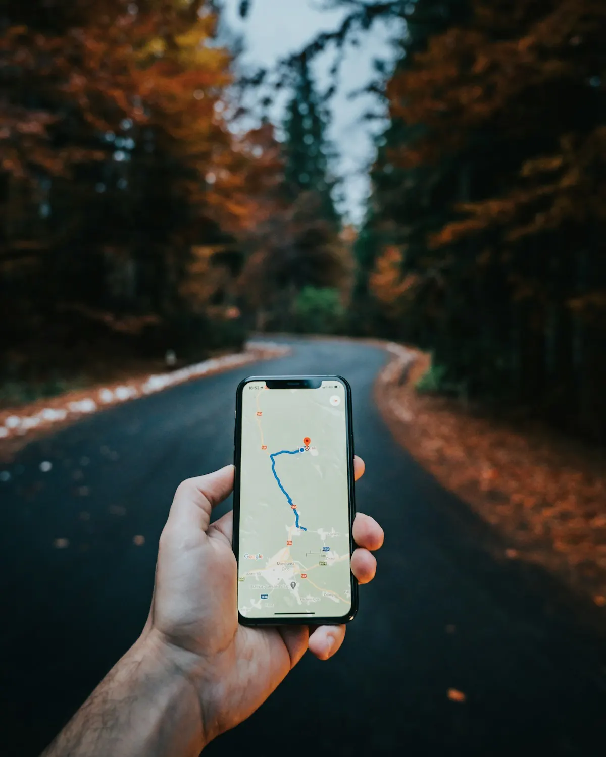 Mão segurando celular com rota no mapa aberta, com estrada ao fundo, representando clientes chegando pelo Google Maps.