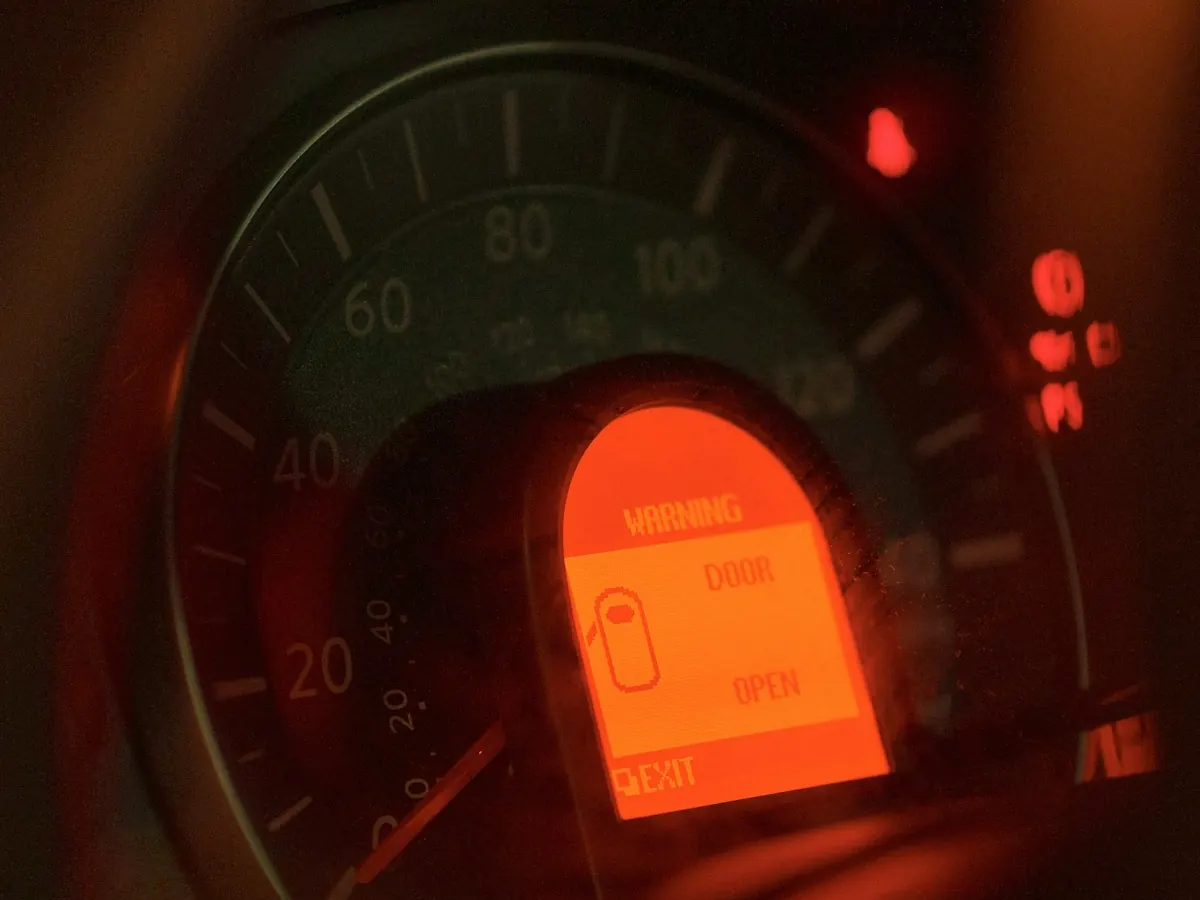 Painel de carro no escuro com o visor laranja aceso mostrando uma mensagem de alerta ao lado do velocímetro.