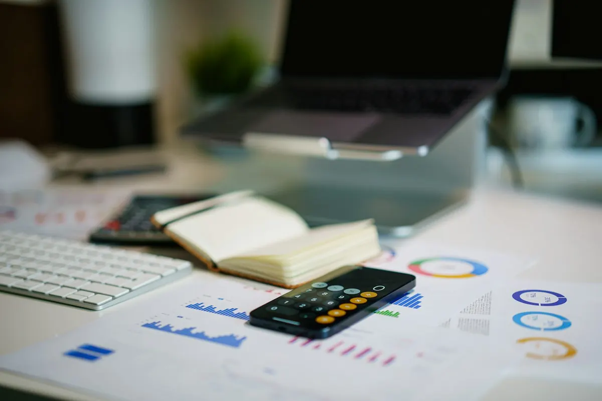 Mesa de escritório com celular, calculadora e gráficos financeiros para planejar o orçamento de anúncios em 2026.
