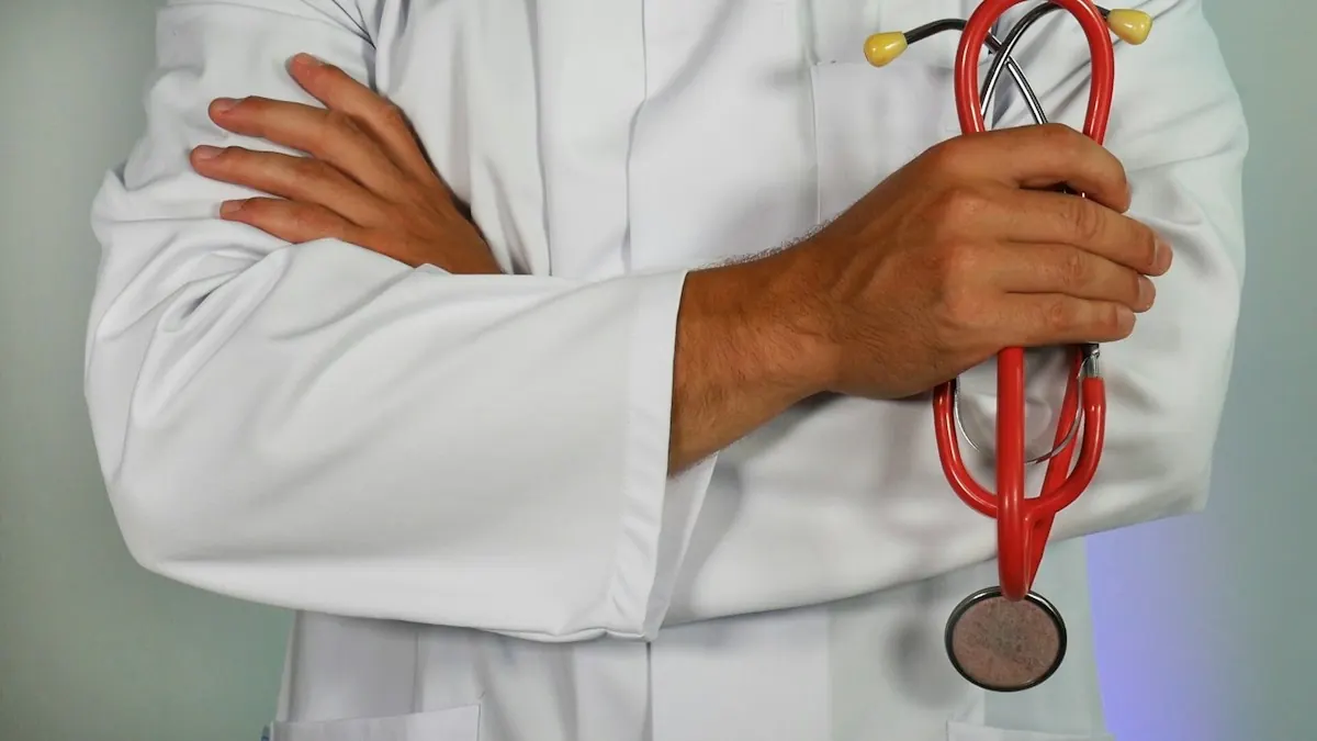 Médico de jaleco branco com os braços cruzados segurando um estetoscópio vermelho.