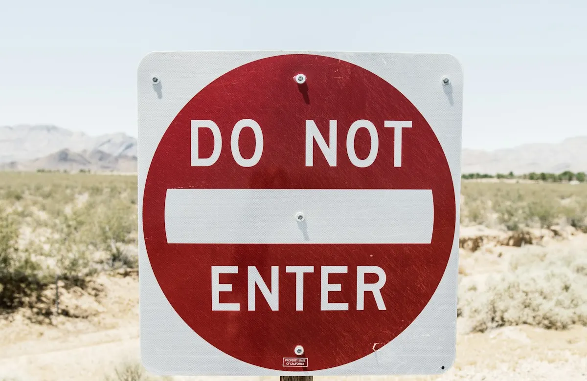 Placa vermelha de trânsito com os dizeres Do Not Enter, proibido entrar, numa estrada de terra.