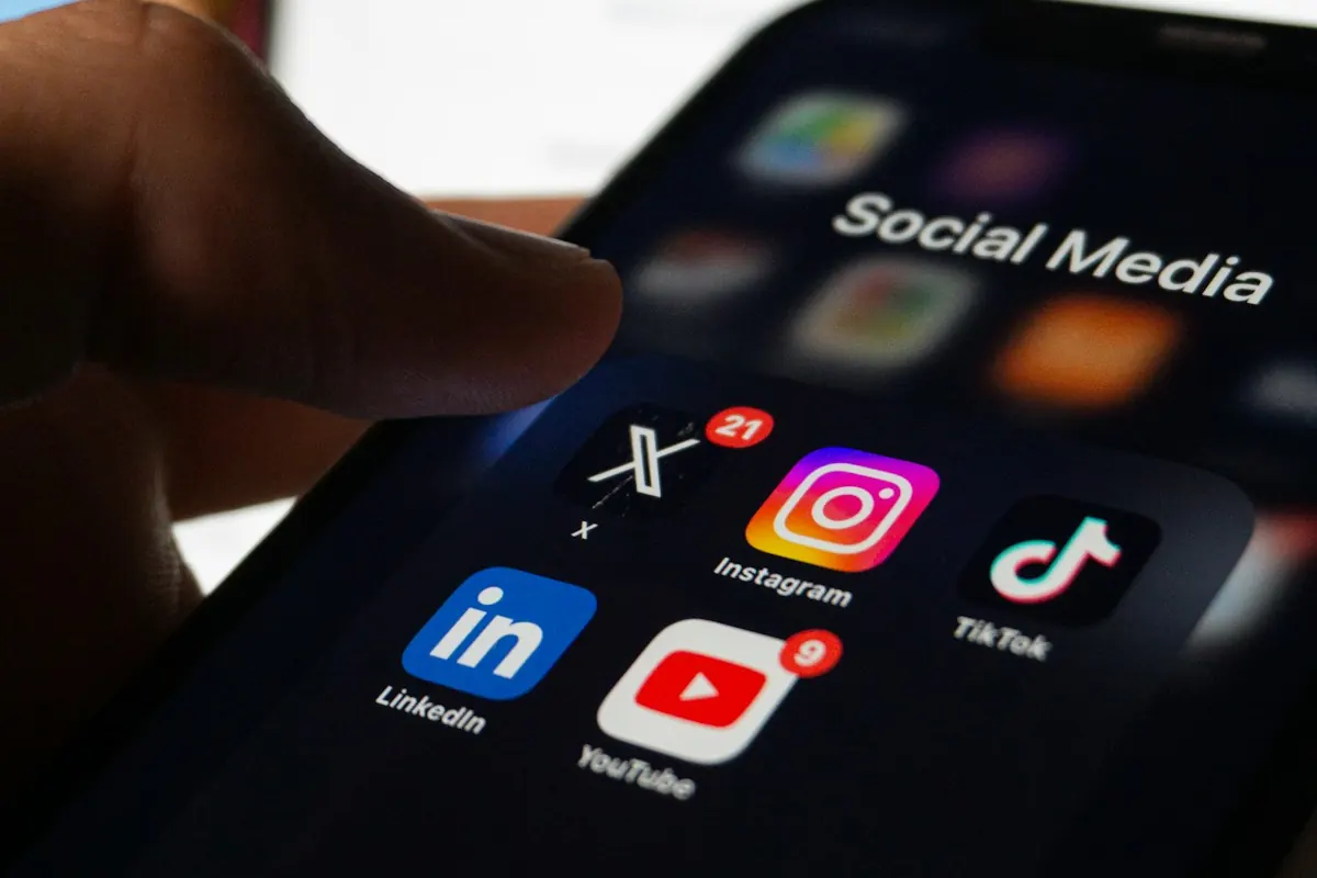 Mão segurando um celular com a pasta de aplicativos de redes sociais aberta, com Instagram, YouTube, LinkedIn e TikTok.