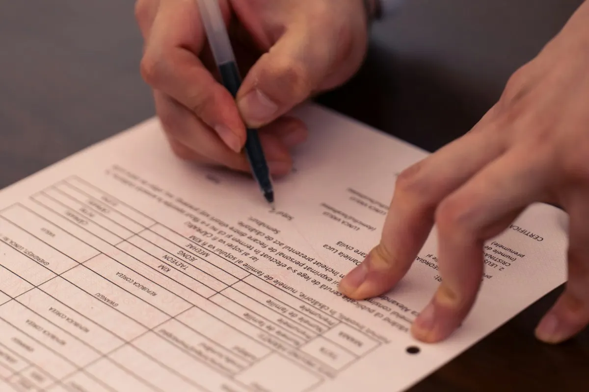 Mãos segurando uma caneta e assinando um documento formal sobre uma mesa escura.