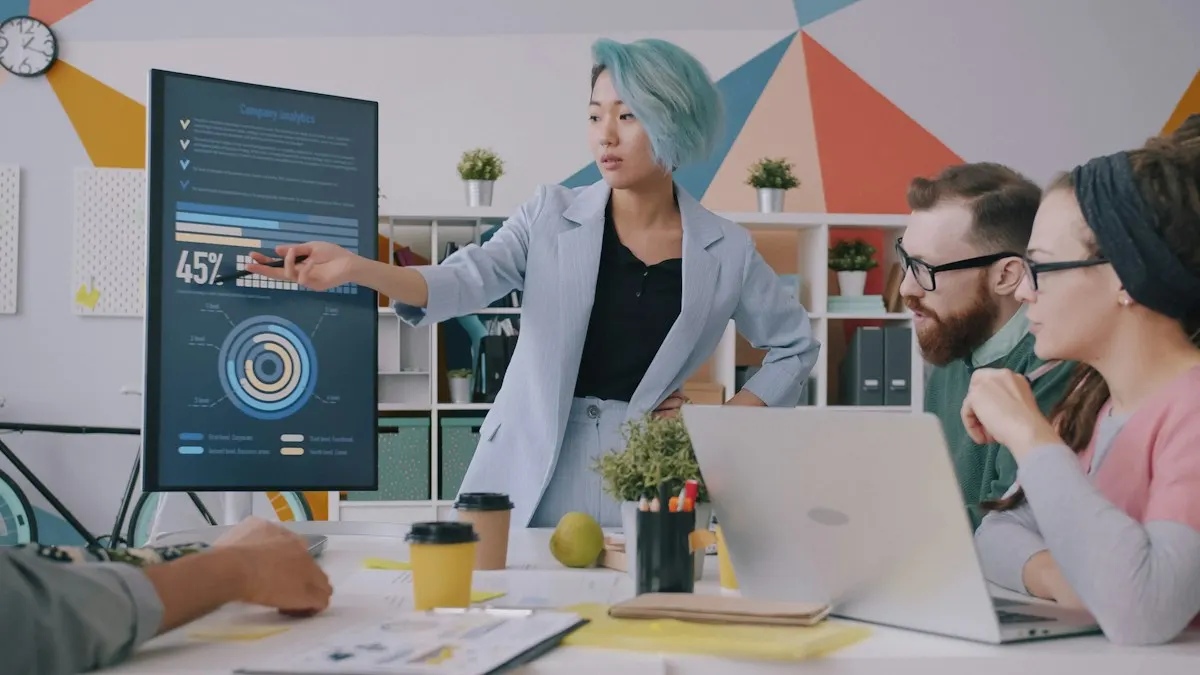 Mulher apontando para um gráfico numa tela grande durante uma reunião com a equipe e notebooks na mesa.