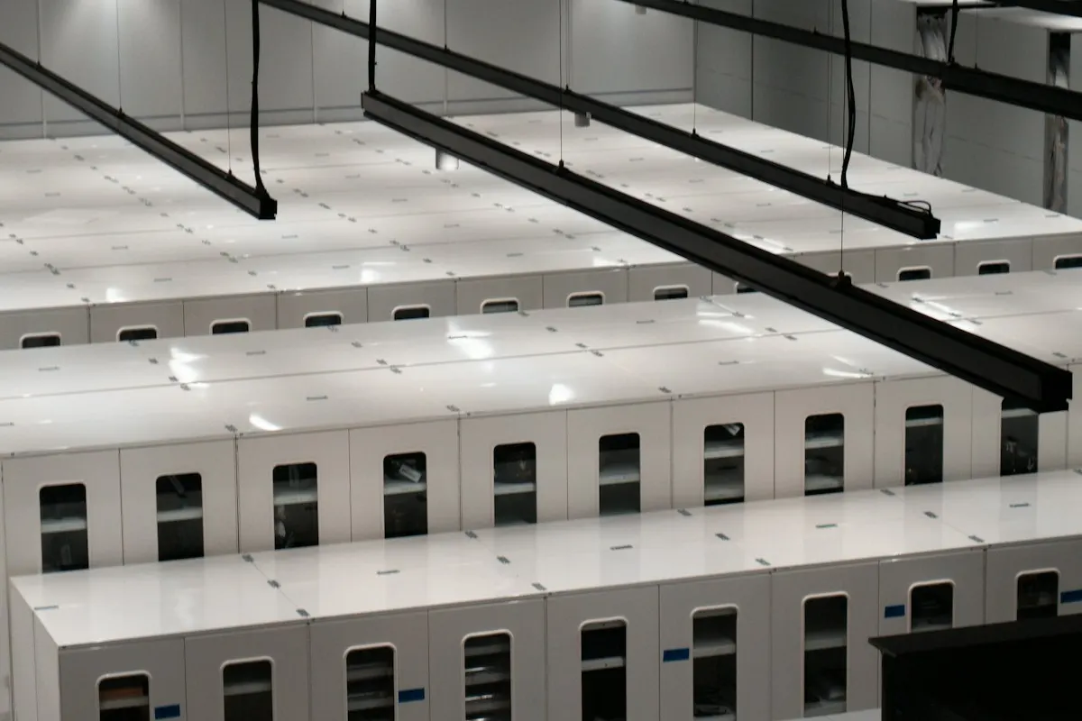 Fileiras de servidores brancos num data center iluminado, com calhas de cabos suspensas no teto.