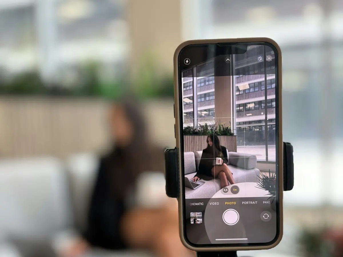 Celular preso num tripé gravando uma mulher sentada no sofá, como numa produção de vídeo para anúncio.
