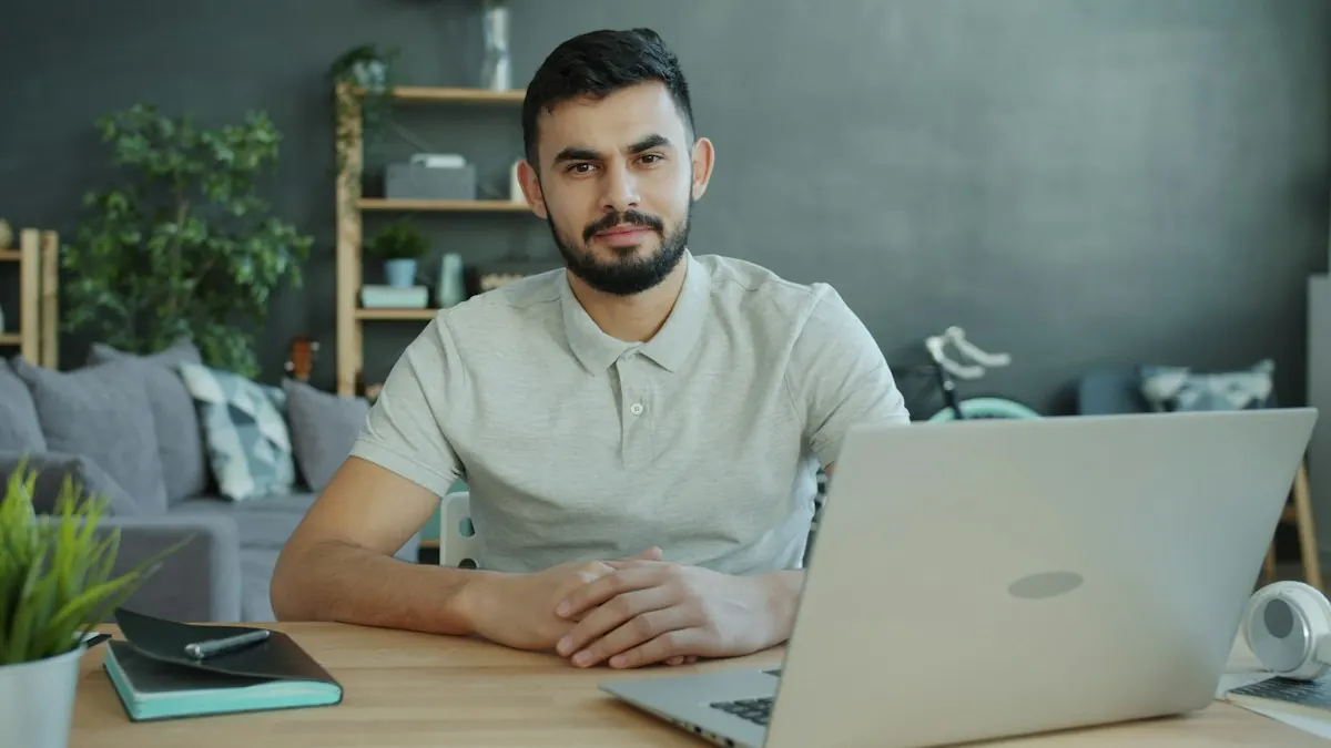 Empresário sorrindo sentado à mesa com o notebook aberto, num escritório em casa com plantas ao fundo.