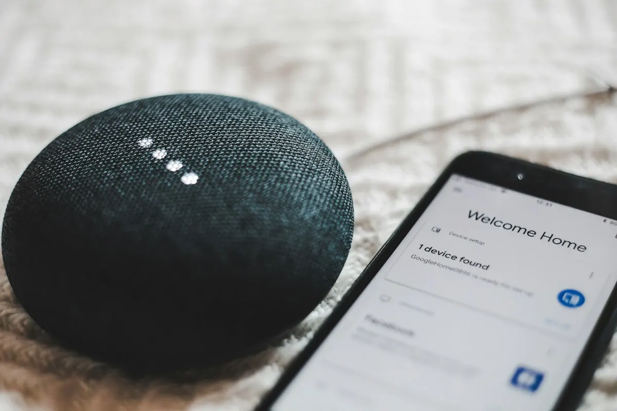 Caixa de som inteligente Google Home Mini ao lado de um celular com o aplicativo Google Home aberto.