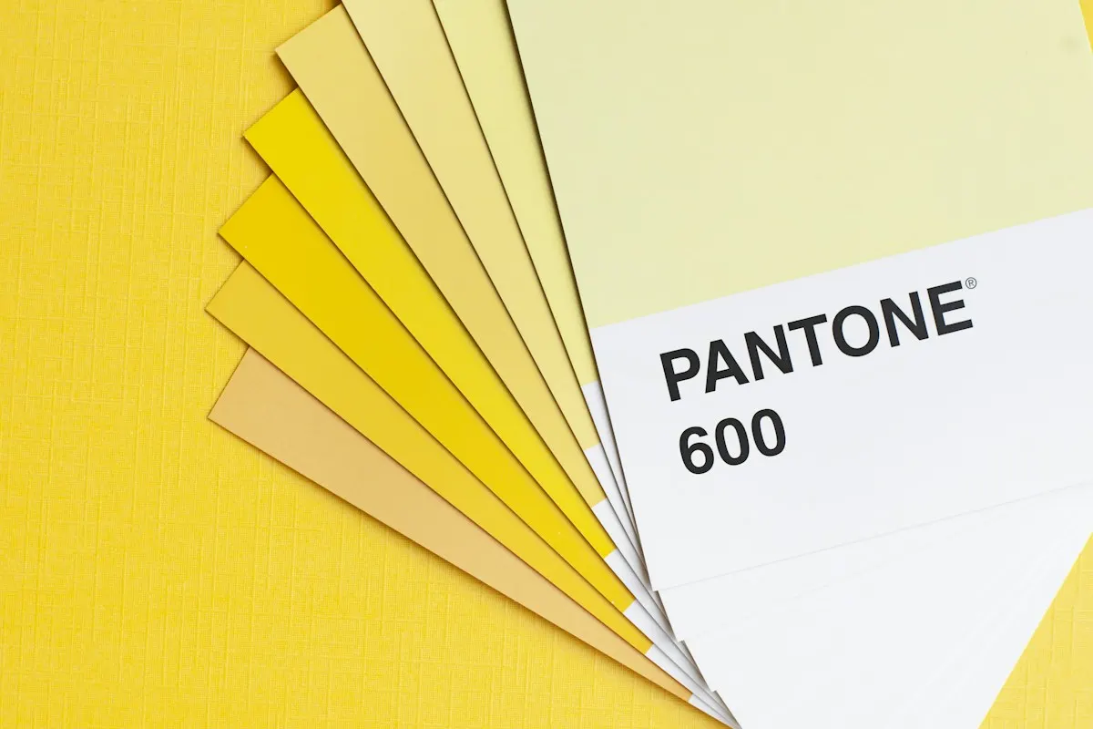 Amostras Pantone em tons de amarelo sobre mesa amarela, mostrando como a mesma cor muda com o contraste ao redor.