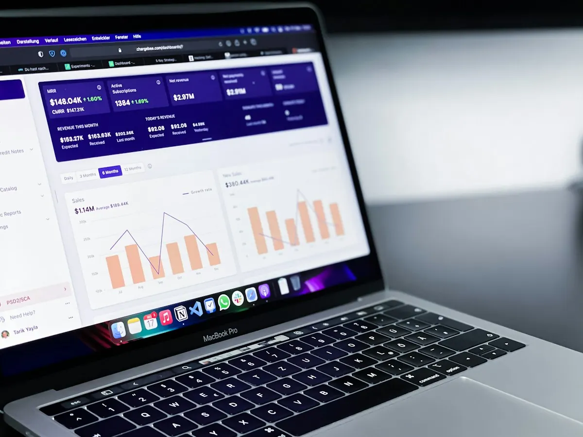 Notebook aberto num painel de vendas com gráficos de barras e de linhas em tons de laranja.