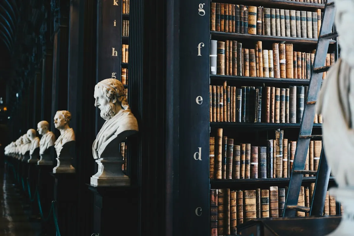 Biblioteca antiga com estantes altas de livros e bustos de mármore enfileirados.