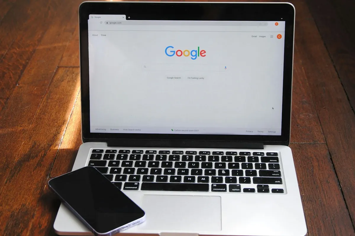 Notebook aberto na página inicial do Google sobre uma mesa de madeira, com um celular apoiado no teclado.