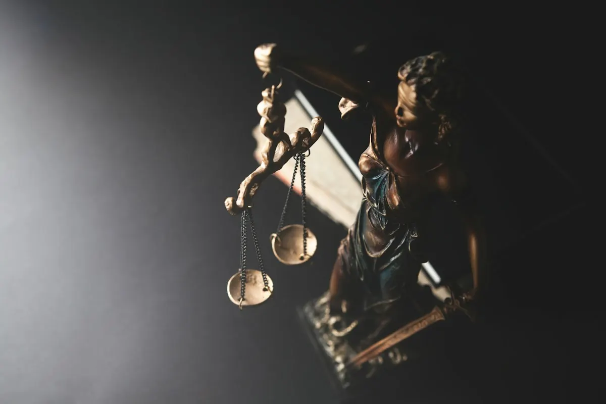 Estátua da Justiça segurando a balança, iluminada sobre um fundo escuro.